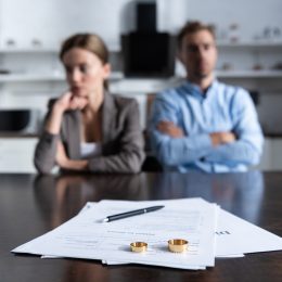 An unhappy couple sitting at a table with divorce documents and their wedding bands.