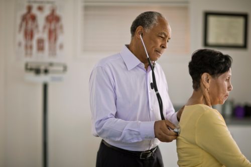 Male doctor listening to the heartbeat of a mature female patient inside his office.