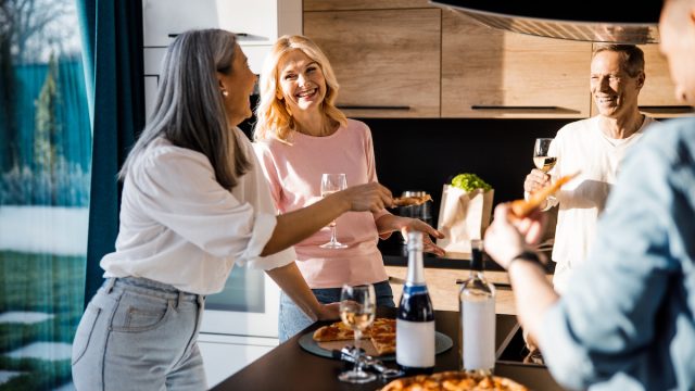 Cheerful men and women drinking wine and chatting in the kitchen