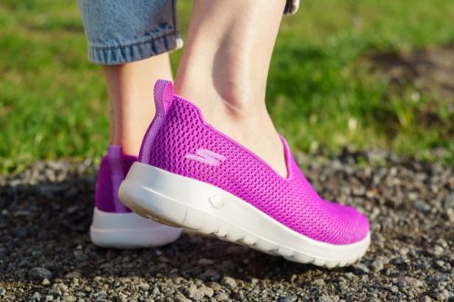 Close up of a woman's ankles and feet wearing fuchsia Skechers Go Walk sneakers outside