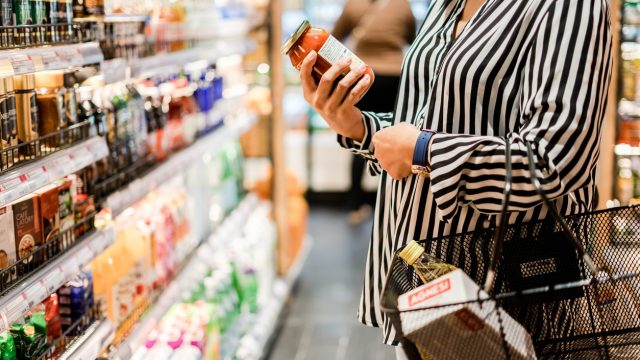 Close up of a person holding a jar and reading the label while shopping in a grocery store