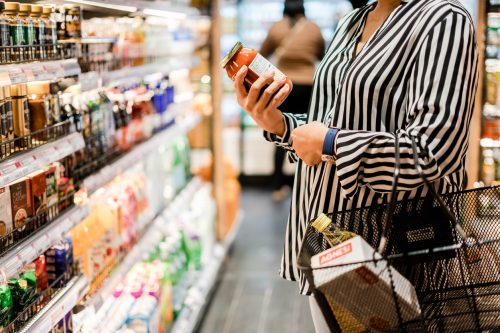 Close up of a person holding a jar and reading the label while shopping in a grocery store