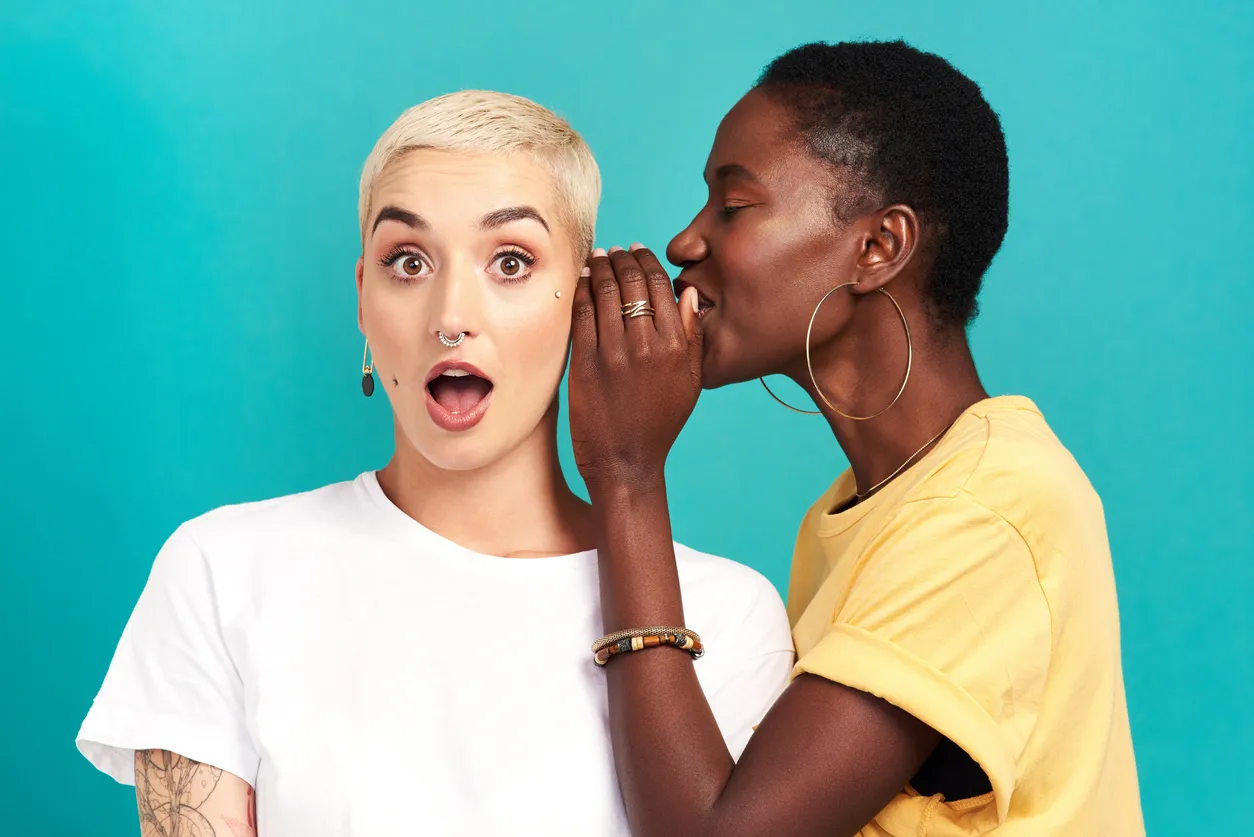 Studio shot of a young woman whispering in her friend’s ear