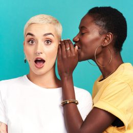 Studio shot of a young woman whispering in her friend’s ear