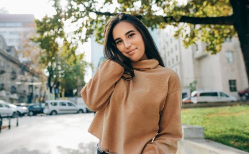 Outdoor image of beautiful young brunette woman wearing beige sweater