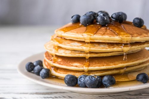 Close up of fluffy pancakes with maple syrup and blueberries