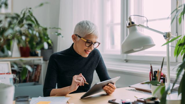 A happy, mature woman sitting at a desk, focused on her work in black turtle neck sweater