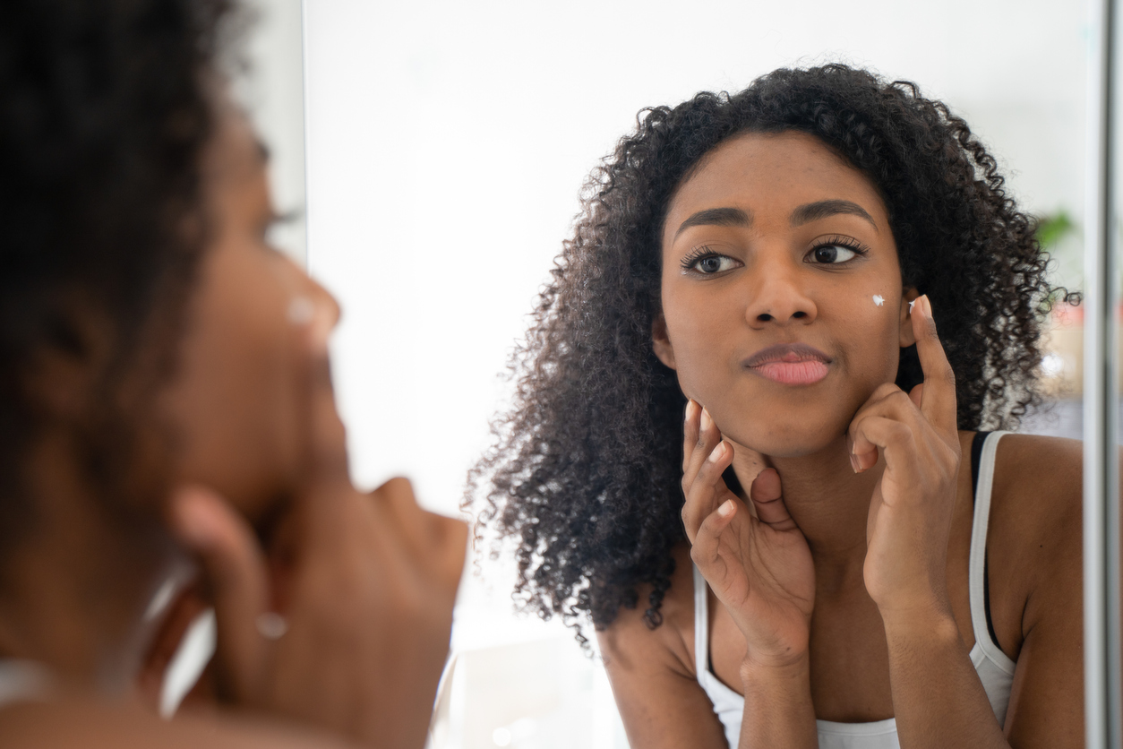 Woman applying skin cream in the bathroom mirror.