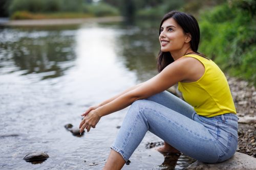 Young woman sitting on rock by a stream with bare feet in water and relaxing