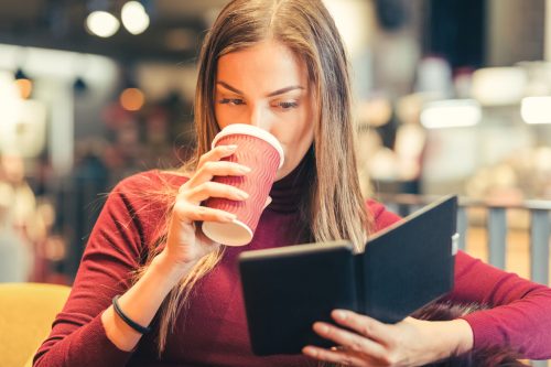 Young woman drinking coffee and reading an e-book