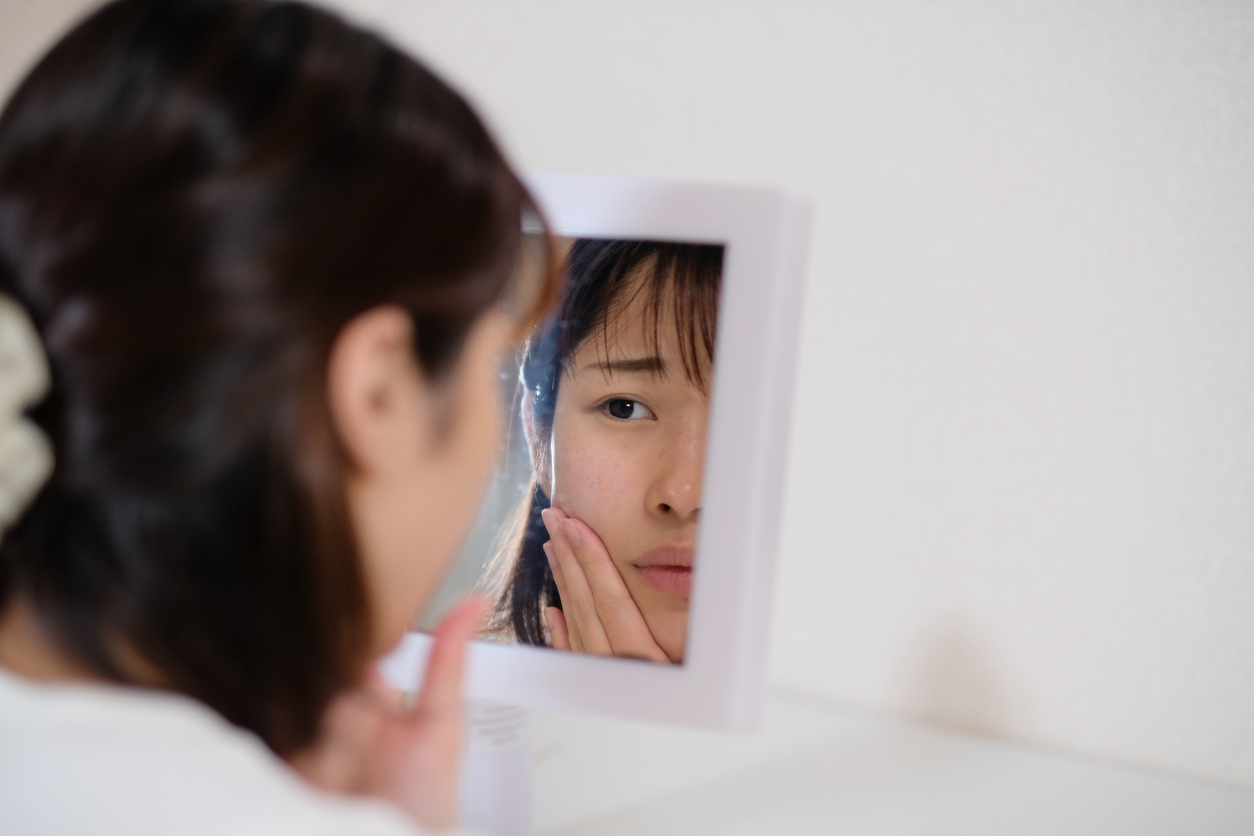 Woman looking at her skin in a mirror. 