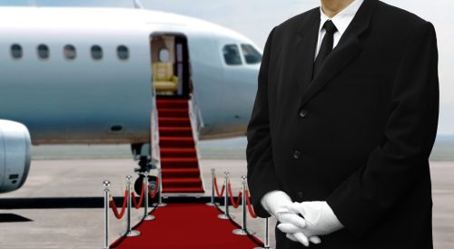 butler standing in front of red carpet leading to private jet