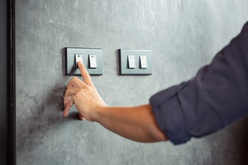 Close up of a person's hand on a light switch that matches the green color of the walls