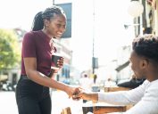A man sitting at an outdoor restaurant table shakes hands with a woman who he's meeting for a first date.