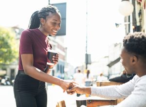A man sitting at an outdoor restaurant table shakes hands with a woman who he's meeting for a first date.
