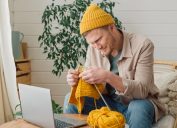 A man watching a video to learn how to knit a yellow scarf to match his yellow hat.