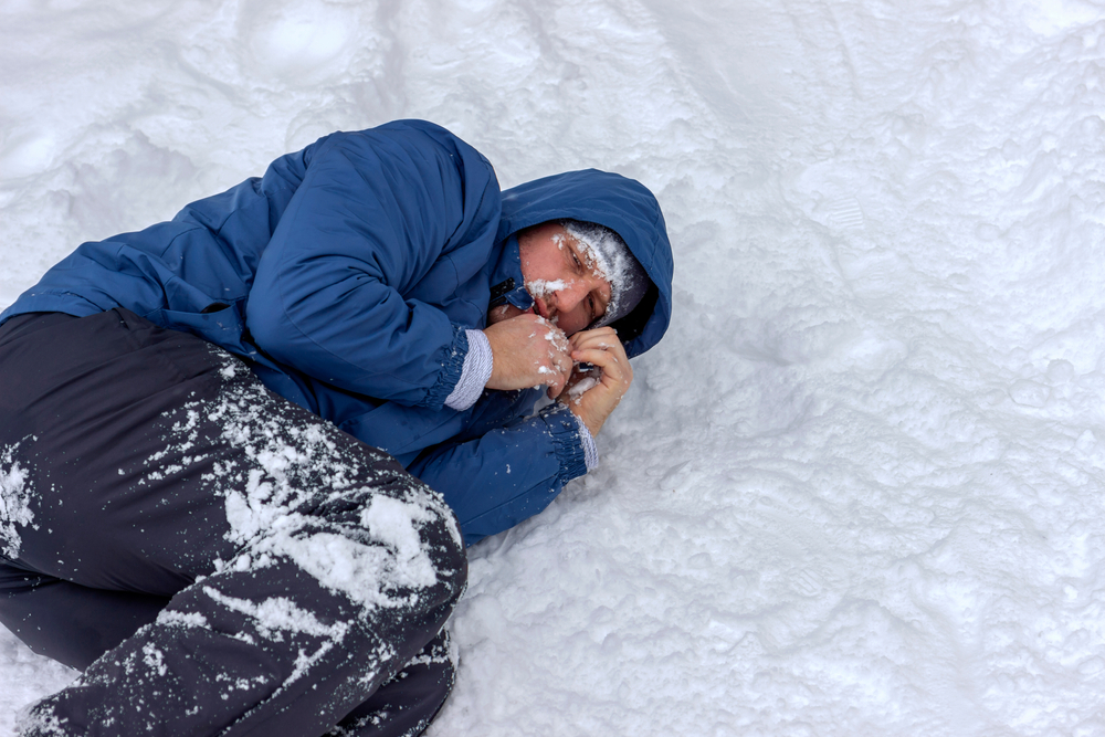 A man in a blue jacket lying the snow and suffering from extreme cold