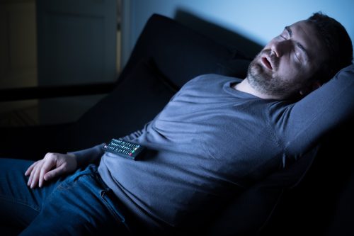 Man sleeping on the couch in front of television screen