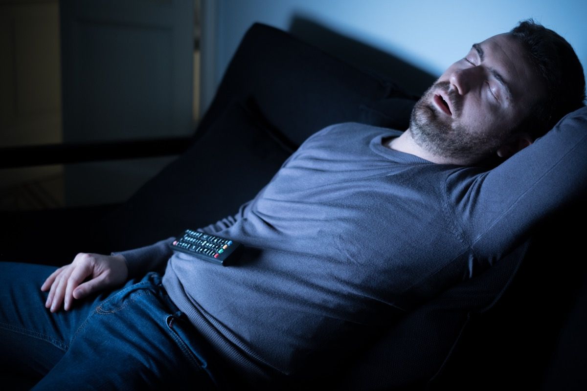 Man sleeping on the couch in front of television screen