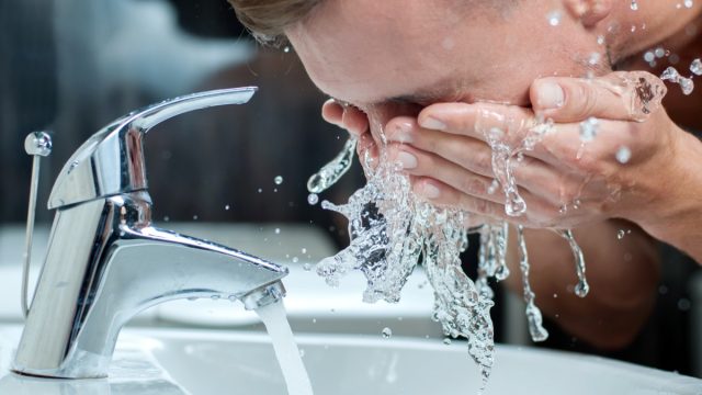 white man washing face in sink