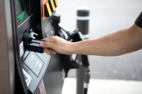 Close up of a person's arm using a credit card to pay for gas at a fuel pump