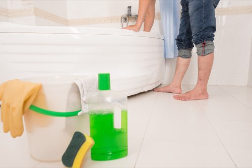 Cropped image of barefoot man cleaning bathtub