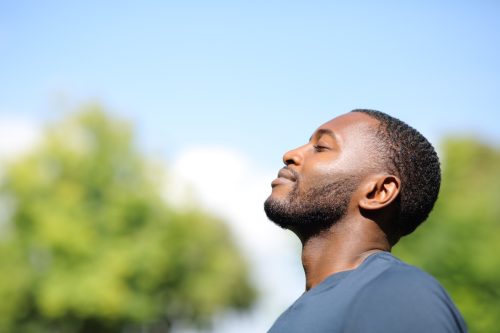 Black man walking outdoors taking a deep breath