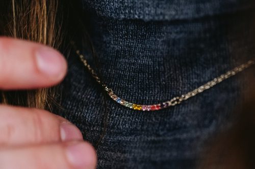Close up of a dainty necklace with multi-colored crystals against a gray sweater