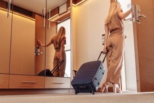 woman in jumpsuit rolling suitcase out of hotel room