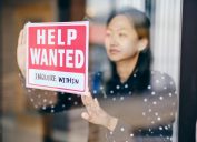 A small business owner, putting up a help wanted sign in her store window.