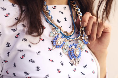 Close up of a brunette woman wearing a pink patterned top and a blue and gold statement necklace
