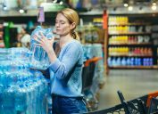 Một phụ nữ trẻ mua một khay nước trong siêu thị.  Anh cầm nó trên tay, xếp vào xe đẩy.  Hoảng loạn trong đại dịch, kiểm dịch.