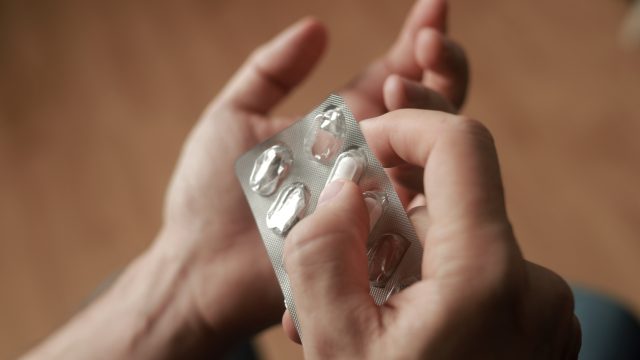 A closeup of hands taking a dietary supplement pill out of a blister pack