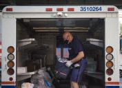 A mail man waring a face mask inside a truck getting ready to deliver.