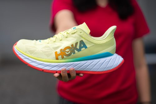 Blurred woman in a red shirt holding a pale yellow Hoka sneaker