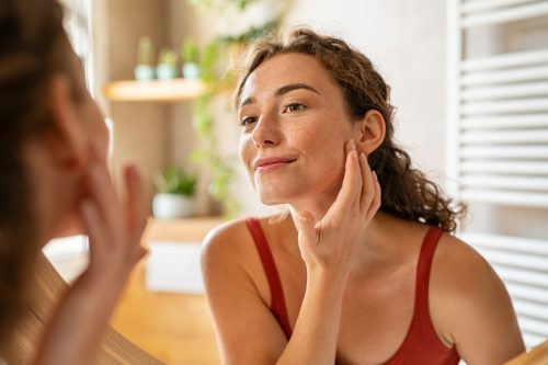 Woman looking at mirror while touching her face and looking at skin