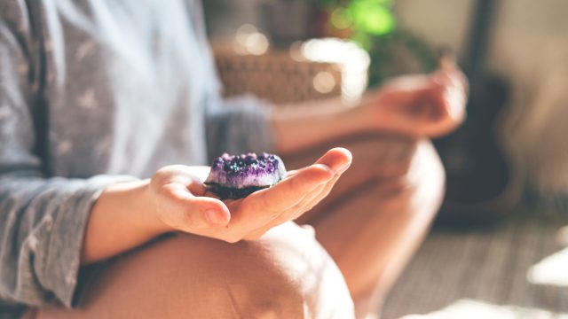 A woman sitting and meditating with a purple crystal in her hand.