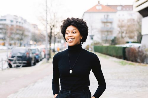 A smiling woman on a city street wearing a black turtleneck.