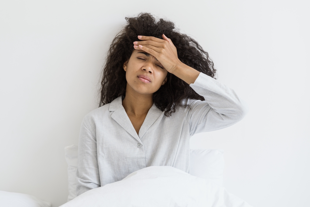 Một người phụ nữ mặc đồ ngủ ngồi trên giường với hai tay đặt trước ngực như thể cô ấy không thể ngủ được