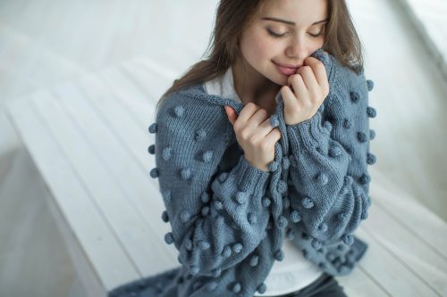 Woman snuggling up in a blue pom-pom sweater.