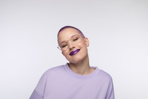 A young woman with short hair dyed purple, wearing purple lipstick and a light purple shirt.