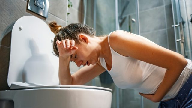 woman with norovirus getting sick in the bathroom over the toilet