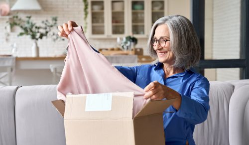 A woman with gray hair takes a shirt out of a box while sitting on her couch