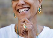 Close up of a smiling woman wearing gold and turquoise matching earrings, rings, and necklaces