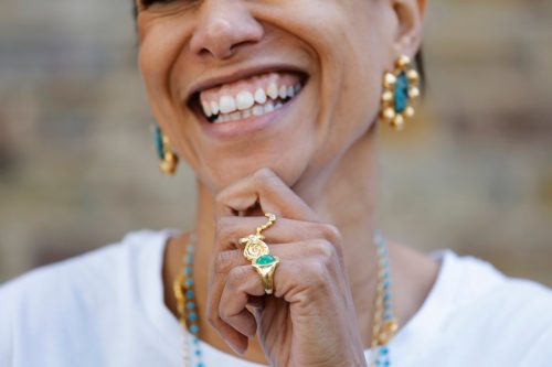 Close up of a smiling woman wearing gold and turquoise matching earrings, rings, and necklaces