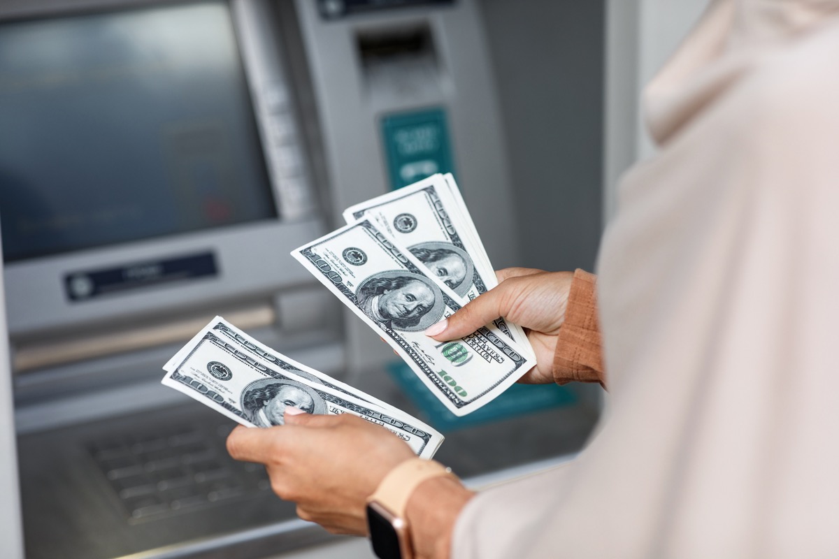 Hands of a person counting hundred-dollar bills in front of an ATM