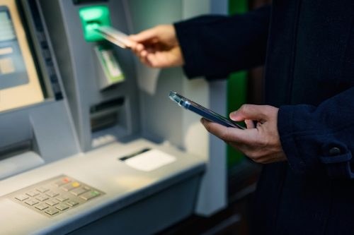 Close up of using cell phone while inserting credit card in ATM machine.