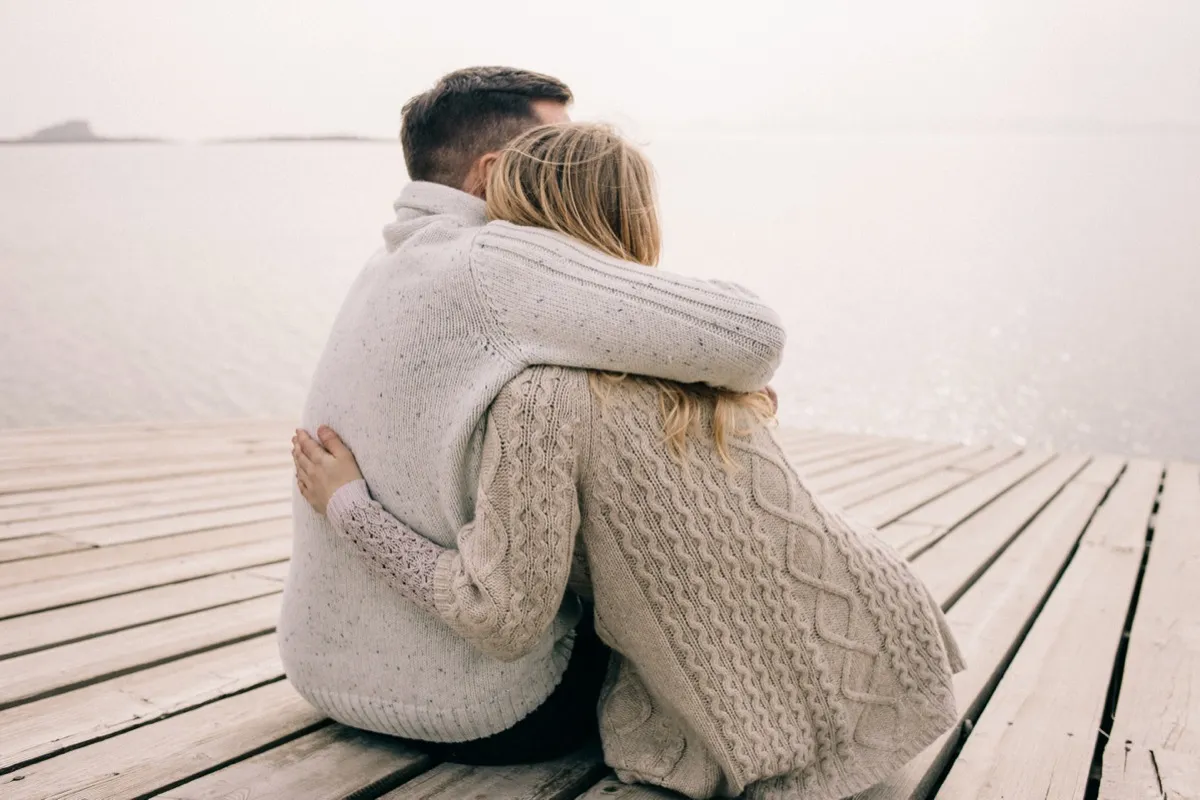 rear view of a Couple Hugging on a Dock, both wearing beige sweaters