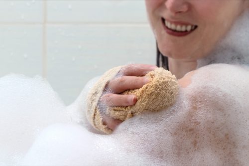 Hand with a washcloth sponge, body in foam of shower gel. Woman taking a shower at bathroom. Life style smiling girl washes in the shower