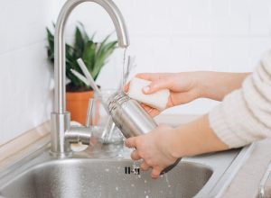 Woman washing a water bottle in kitchen sink